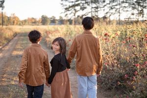 A couple in matching brown jackets walking together on a dirt path during golden hour sunset.