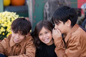 Three young friends in brown jackets share a candid moment together with yellow flowers in the background.