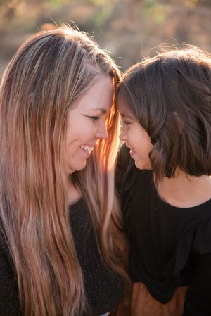 Two people with long hair share a tender moment in warm sunlight against a dark background.