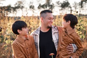A family wearing brown and black outfits poses together outdoors during golden hour for a casual autumn photoshoot.