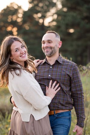 A couple shares a joyful moment together outdoors during sunset, wearing casual fall attire.
