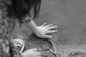 Small hands explore and play with wet sand and mud in a sensory learning activity outdoors.