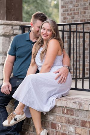 Couple sits close together on a brick ledge with metal railing during an outdoor photo session.