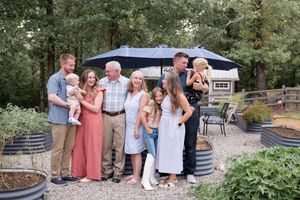 Family members gather outdoors near a patio area for a casual celebration with tables and chairs.
