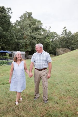 A couple walks hand in hand on a grassy hillside during a sunny afternoon in a park setting.