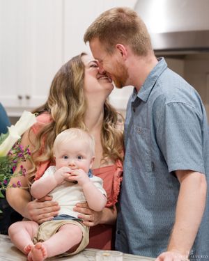 A sweet family moment in the kitchen with a baby between parents sharing a tender kiss.