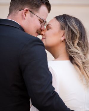 A romantic portrait of a newlywed couple sharing an intimate kiss at a wedding, bride in white and groom in black suit.