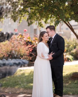 A romantic outdoor wedding moment captured under a tree with soft autumn light in a garden setting.