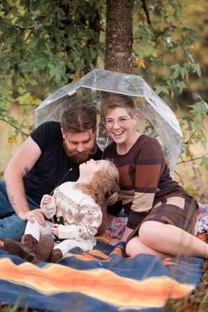 A couple shares an intimate moment on an orange blanket under a tree with clear umbrellas.