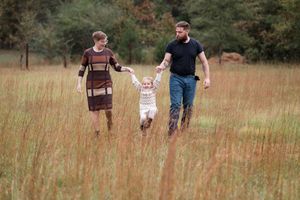 A family walks together through a tall grass field on an autumn afternoon.
