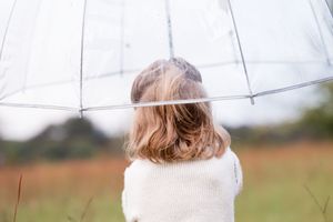 Back view of someone holding a clear umbrella in a field wearing a white sweater.