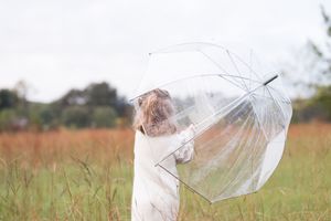 Person in white holding a transparent umbrella in a golden autumn field.