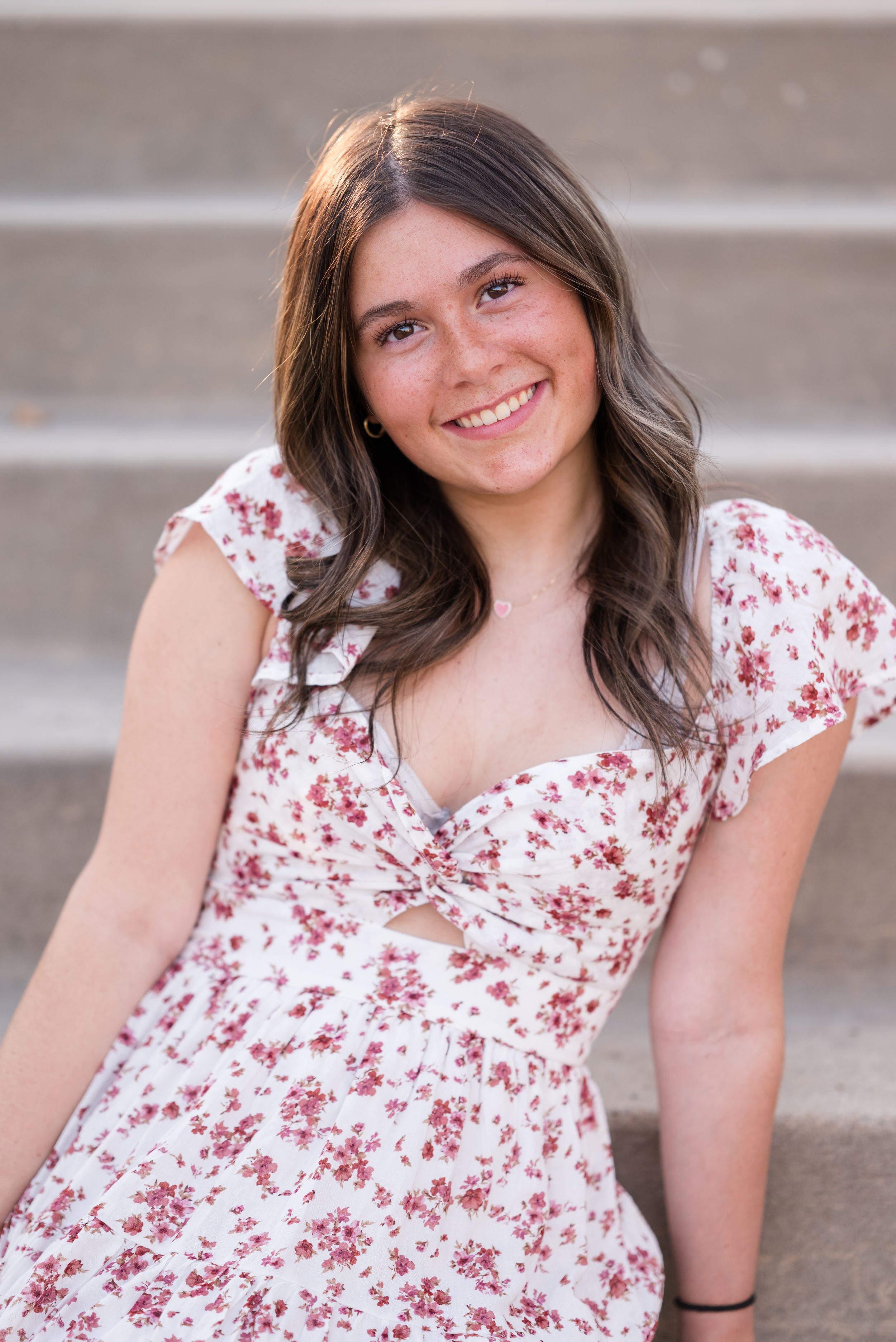 A floral print white dress with red flowers is worn in a casual portrait session on concrete steps.