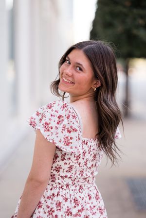 Person in white floral dress twirls and poses against white architectural backdrop.