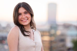 A woman in a beige sweater smiles warmly while posing outdoors during golden hour.
