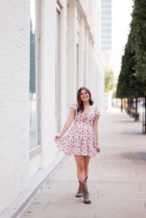A person in a floral dress walks along a white columned building during an outdoor photoshoot.