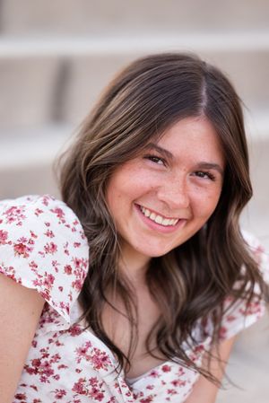 A candid portrait shows a person in a white and red floral dress smiling warmly at the camera.