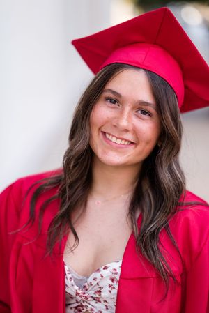 Graduate in bright red cap and gown smiles warmly against light background.