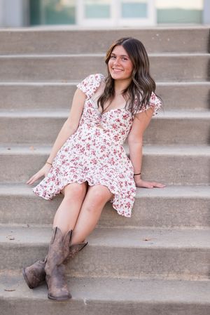 A person in a floral dress and brown boots reclines on concrete steps during a photo session.