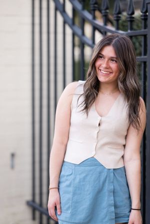 A woman wearing a cream and blue color block top poses against an iron fence backdrop.
