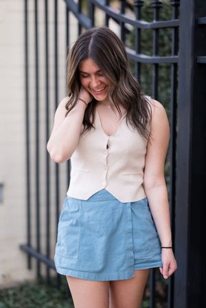 A casual summer outfit featuring a cream sleeveless top and light blue shorts against an iron gate backdrop.