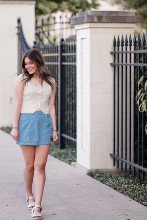 A casual summer outfit featuring light blue shorts and white top photographed on a sidewalk with decorative iron fencing.