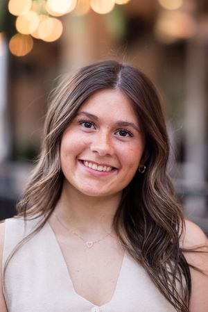 Close-up portrait featuring a delicate necklace and cream colored top with bokeh lighting effects in background.