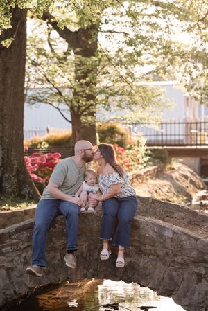 A family sits together on a stone bridge during golden hour sunlight in a garden setting.
