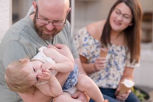 A parent holds and kisses a newborn baby while sitting on a couch at home.