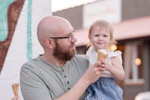 People enjoying ice cream cones while sitting at outdoor tables on a warm evening.