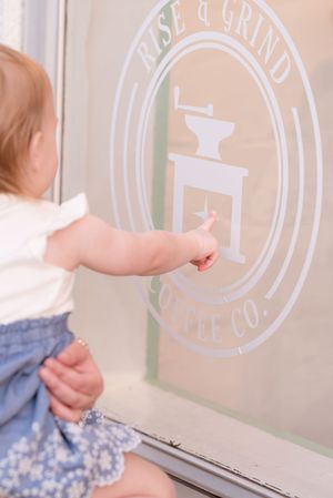 Small child in a blue dress points at a white circular logo design on a glass window or surface.