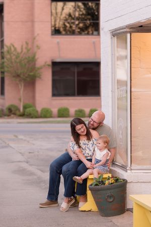 Family sitting together on a porch bench sharing a tender moment in front of a white building exterior.