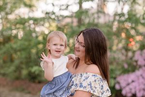 A mother and child share joyful moments together in a garden setting with blooming flowers.