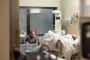 Medical professional in protective gear checking on patient in hospital bed during healthcare visit.