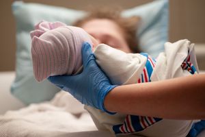 Tiny feet of a newborn wearing pink and blue striped clothing and a pink hat while resting on a bed.