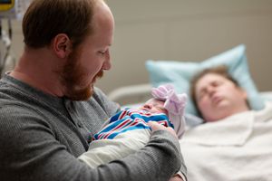 A tender moment as a bearded father in grey sweater holds his newborn baby in striped clothing.