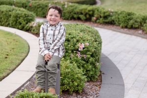 A plaid button-up shirt and gray pants outfit pictured on a curved garden pathway with manicured shrubs.