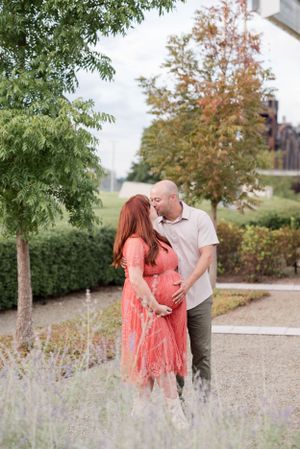 Expecting couple sharing a tender moment in a garden setting with trees and lavender plants.