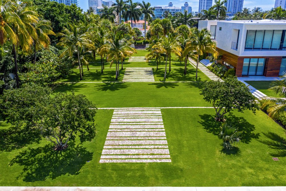 Modern waterfront property with manicured lawn and palm trees featuring a geometric stone pathway in Miami.