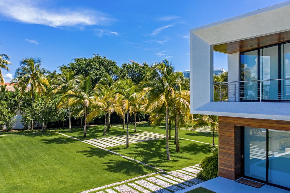 Luxurious modern home with manicured lawn and palm tree landscaping against bright blue sky.