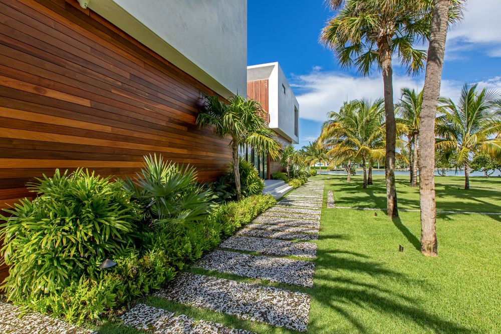 Modern walkway with wood paneling and tropical plants leading through manicured grounds.