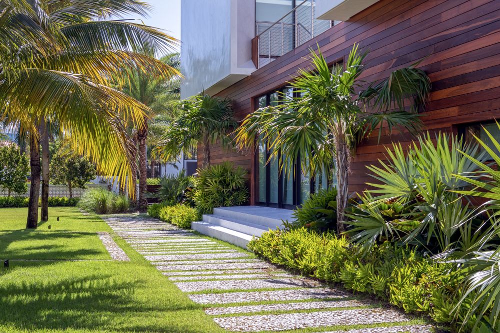 Stone pathway leading to modern home entrance with tropical landscaping and wood accents.
