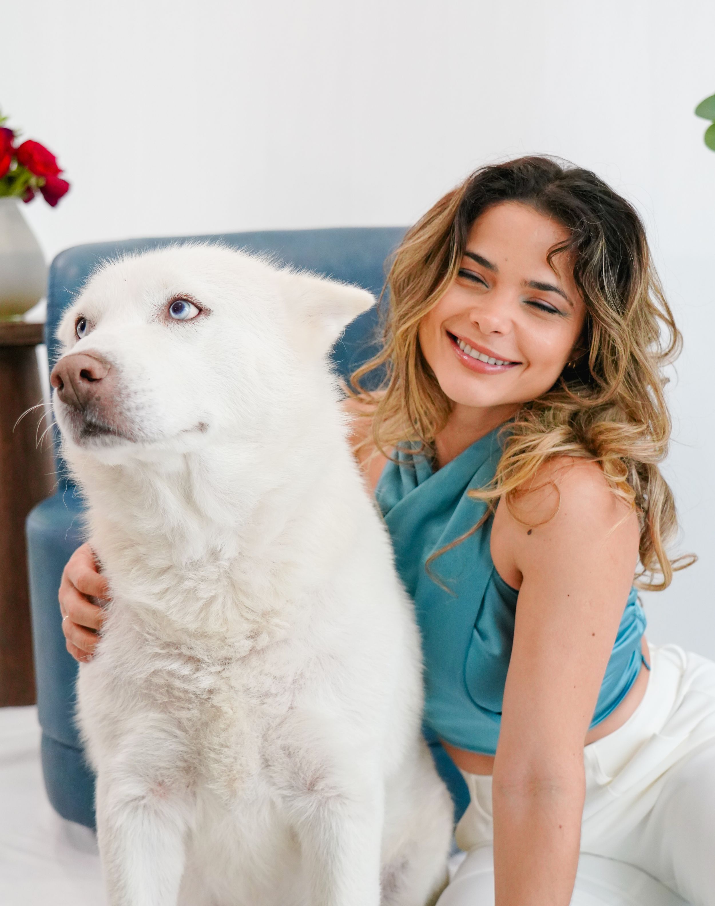 Beautiful white dog poses with companion in studio with red roses and greenery.