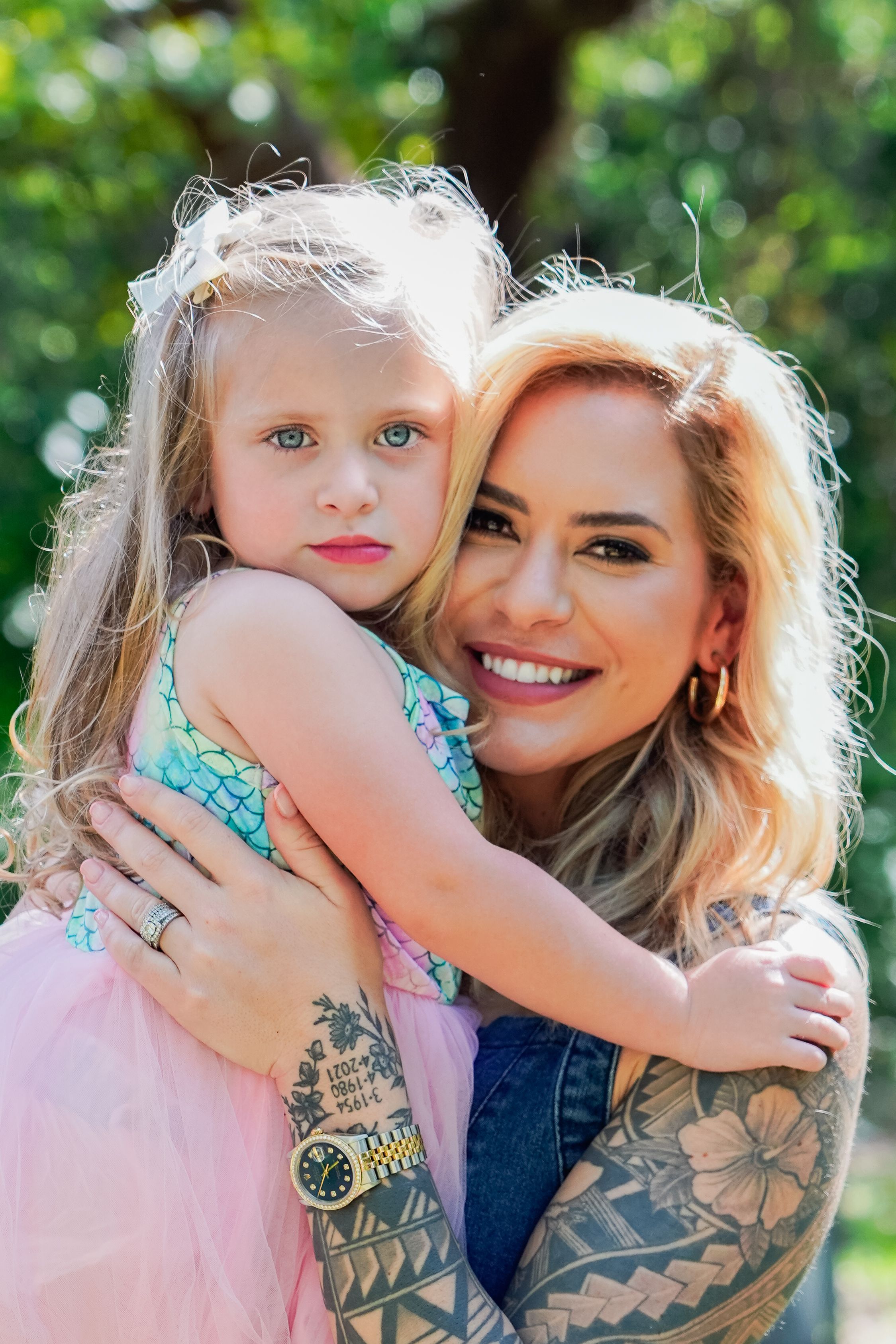 Close up portrait of parent and child with tattoos and smiles in a sunny outdoor setting.