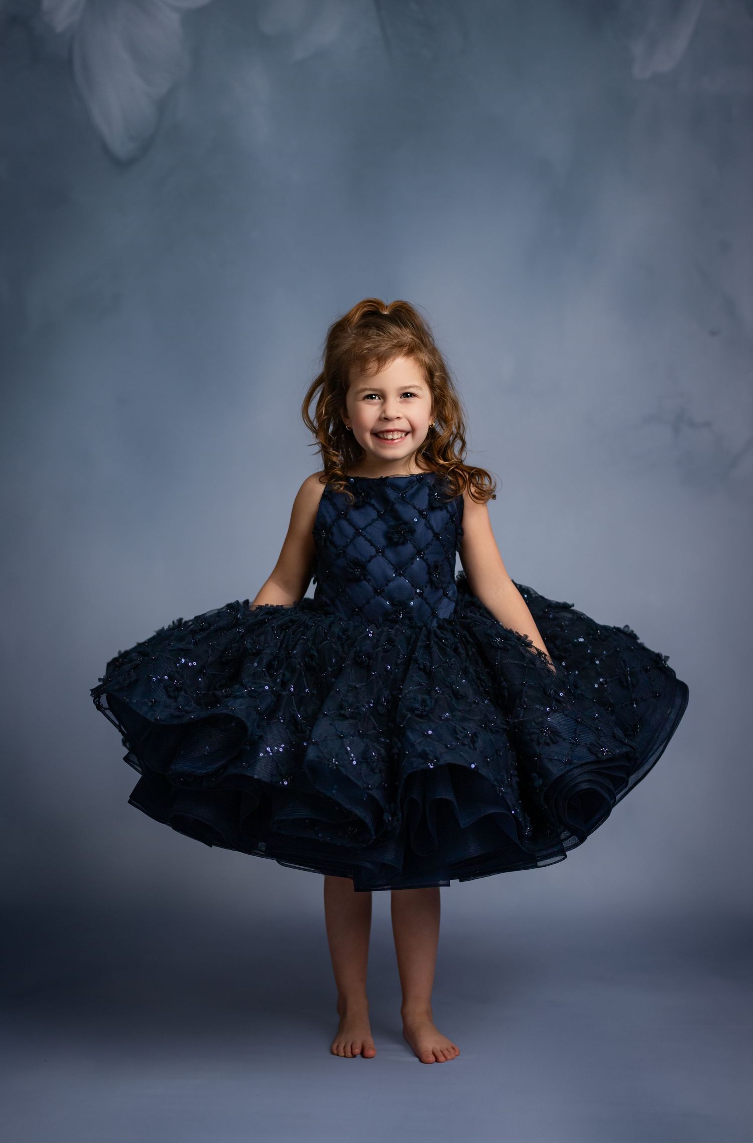 Twirling portrait in navy tea-length dress with floral hair accessory against moody backdrop.