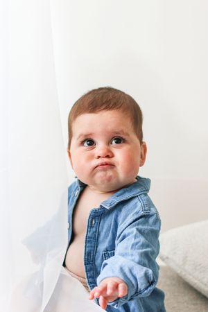 Baby wearing unzipped denim shirt showing an adorable pout expression against white wall background, during shoot in Nottingham