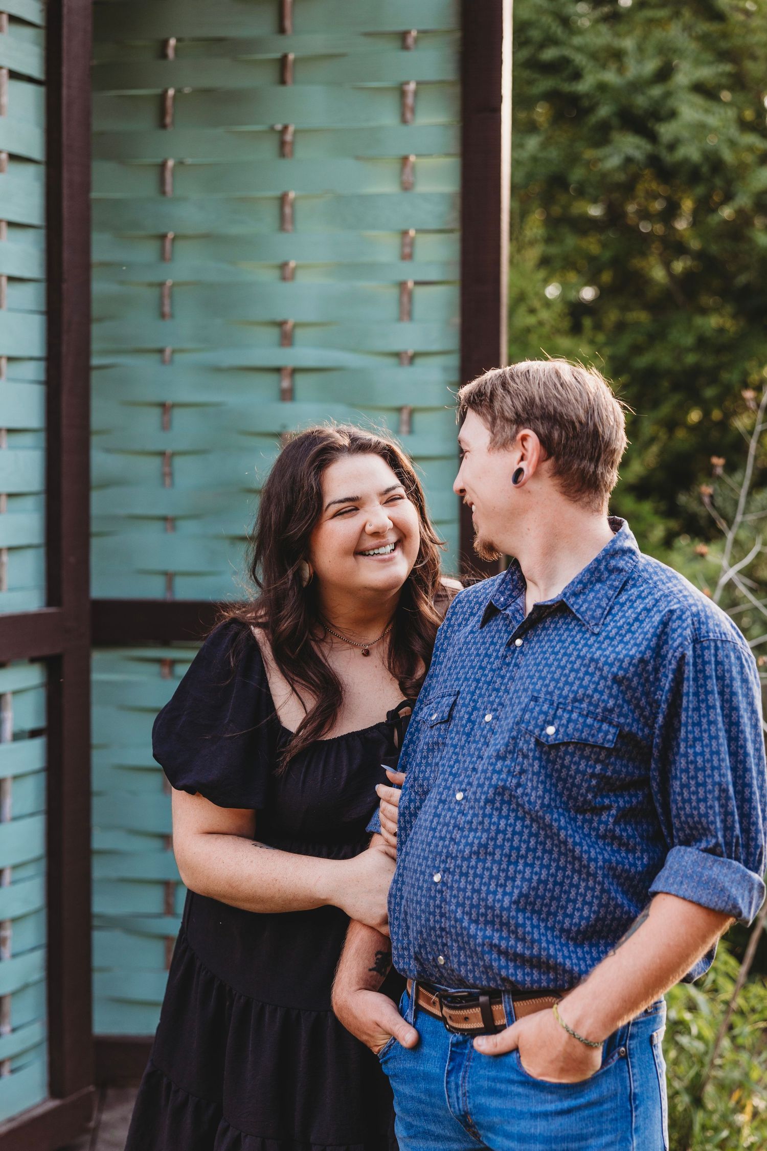 Couple sharing playful moments against turquoise wall outdoors.