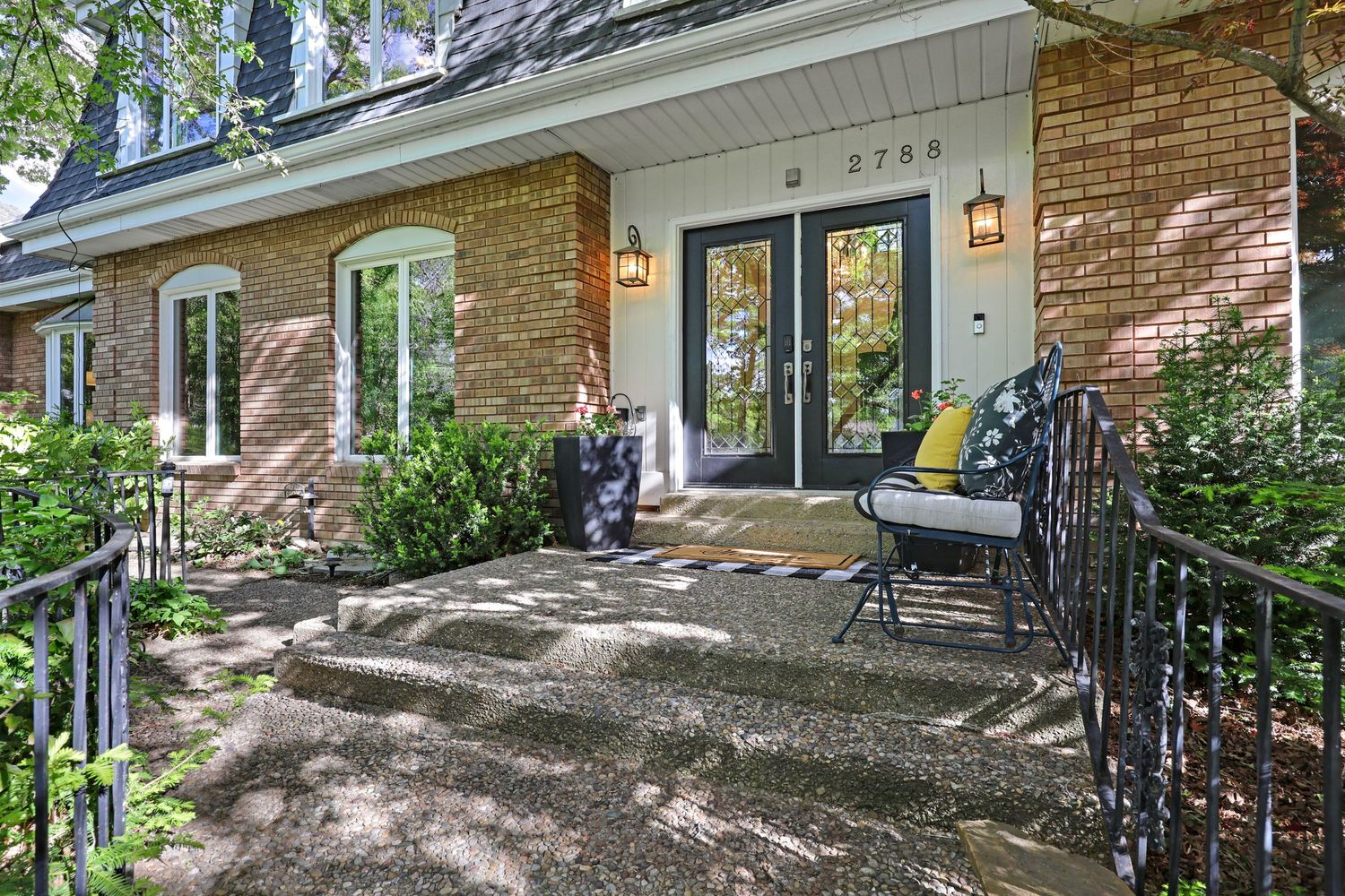 Charming brick home entrance with French doors, number 2799, lush greenery, and decorative iron railings.