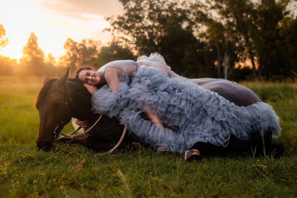 Ethereal maternity photoshoot with a horse in a sunlit meadow at golden hour.