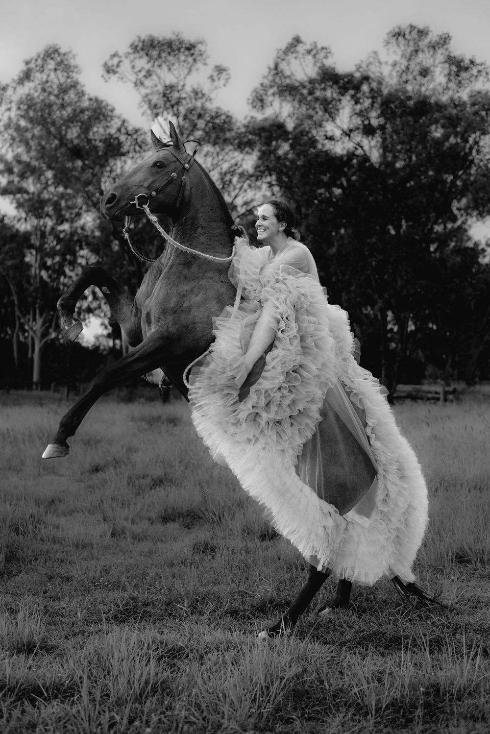 A vintage black and white photo showing someone in a flowing dress riding a rearing horse.